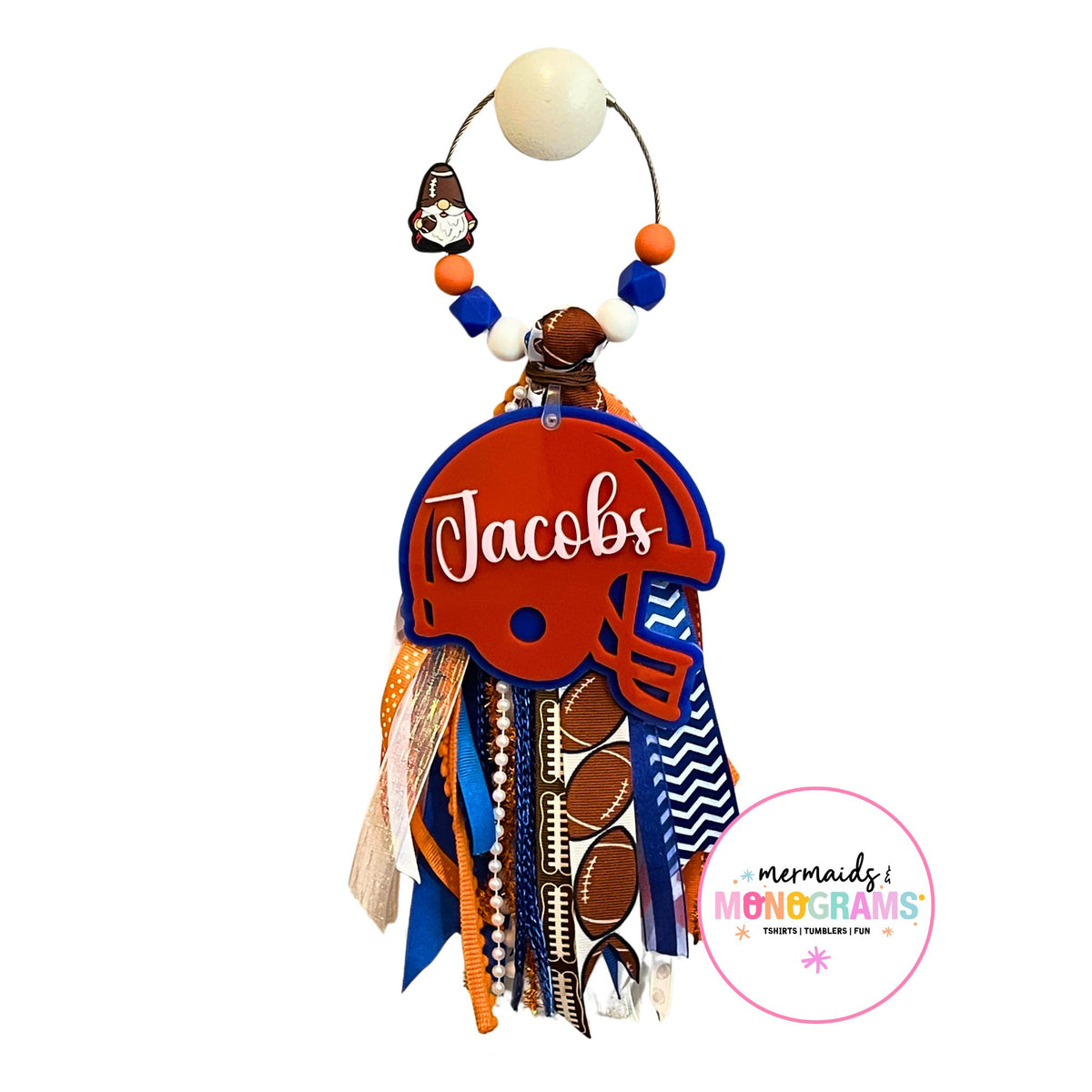 Custom football helmet bag tag with name “Jacobs” in white script on orange helmet, hanging with blue and orange ribbon tassel