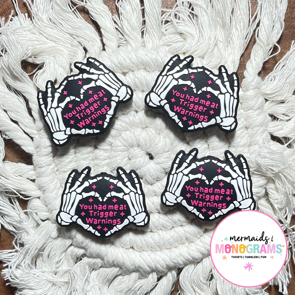 Four skeleton hand beads with text on a textured white surface, featuring the brand 'Mermaids & Monograms'.